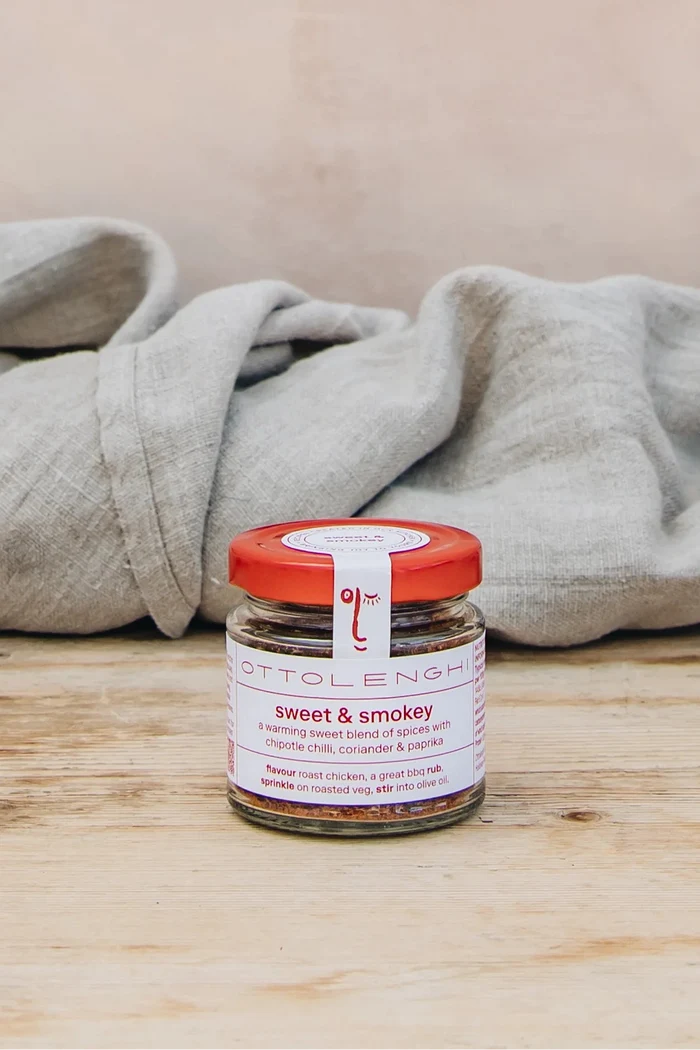 Jar of 'sweet & smoky' seasoning on a wooden surface with a beige blanket in the background