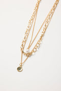 Gold triple-layer necklace with mixed chains, a pearl accent, and a round gold disc charm, styled flat on a white background