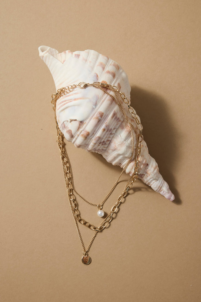 Gold triple-layer necklace with mixed chains, a pearl accent, and a round gold disc charm