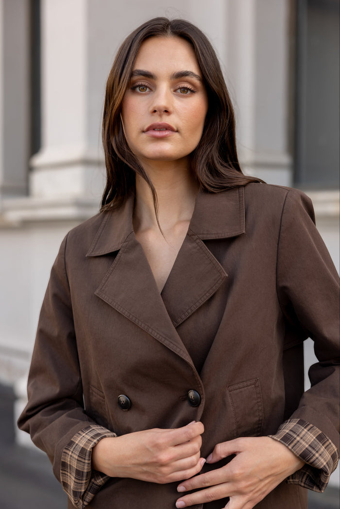 Woman wearing a brown coat with a blurred architectural background