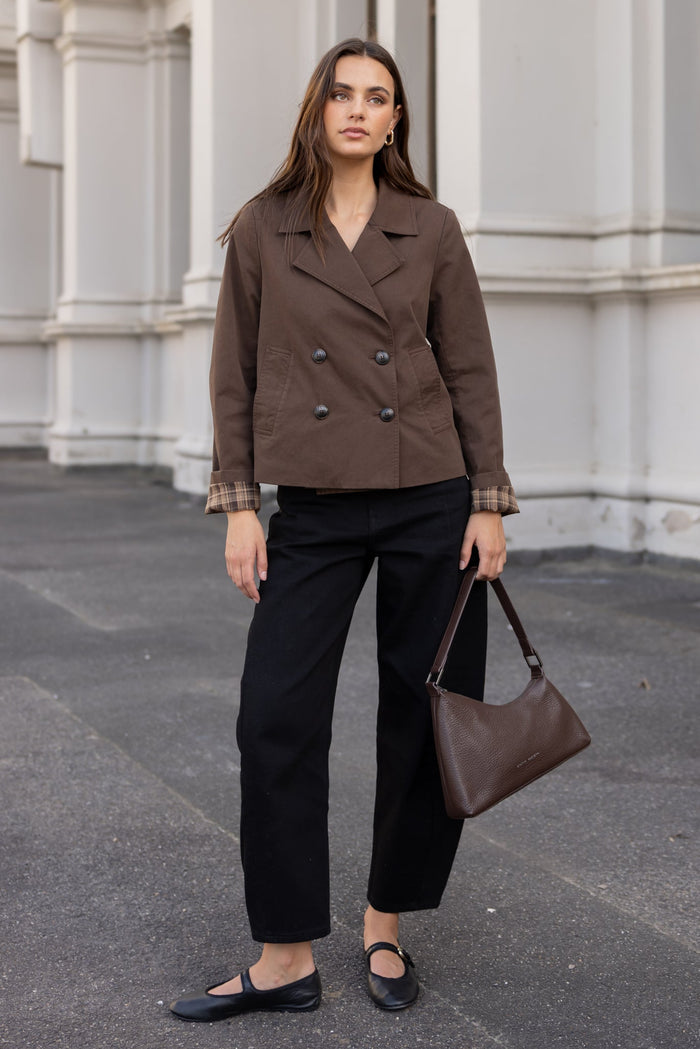 Woman in a brown coat and black pants standing in front of a building