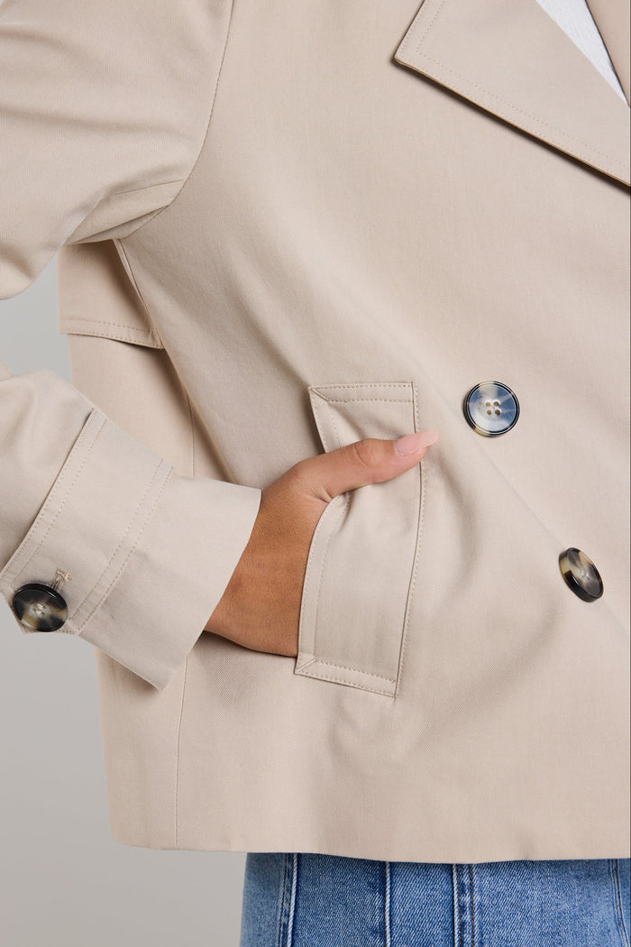 Model wears a cropped trench in a taupe beige, featuring collared neckline and buttons
