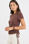 Woman wearing a fitted chocolate brown short sleeve tee with ribbed texture and adjustable side ruching, paired with high-rise cream jeans.