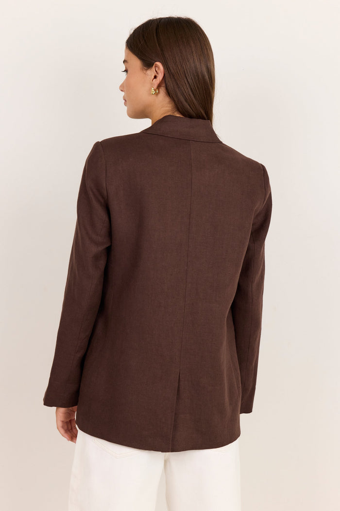 A woman shown from the back wearing a dark brown tailored blazer and white pants, photographed against a plain light beige studio background.
col_pattern
