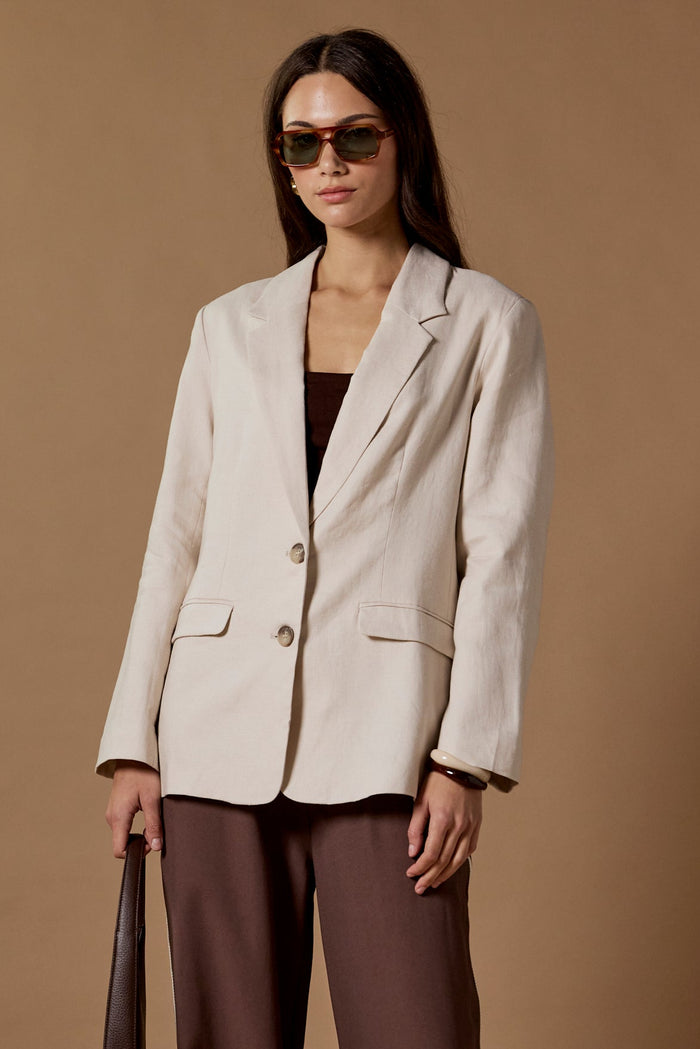 Woman wearing a beige blazer and brown pants against a brown background