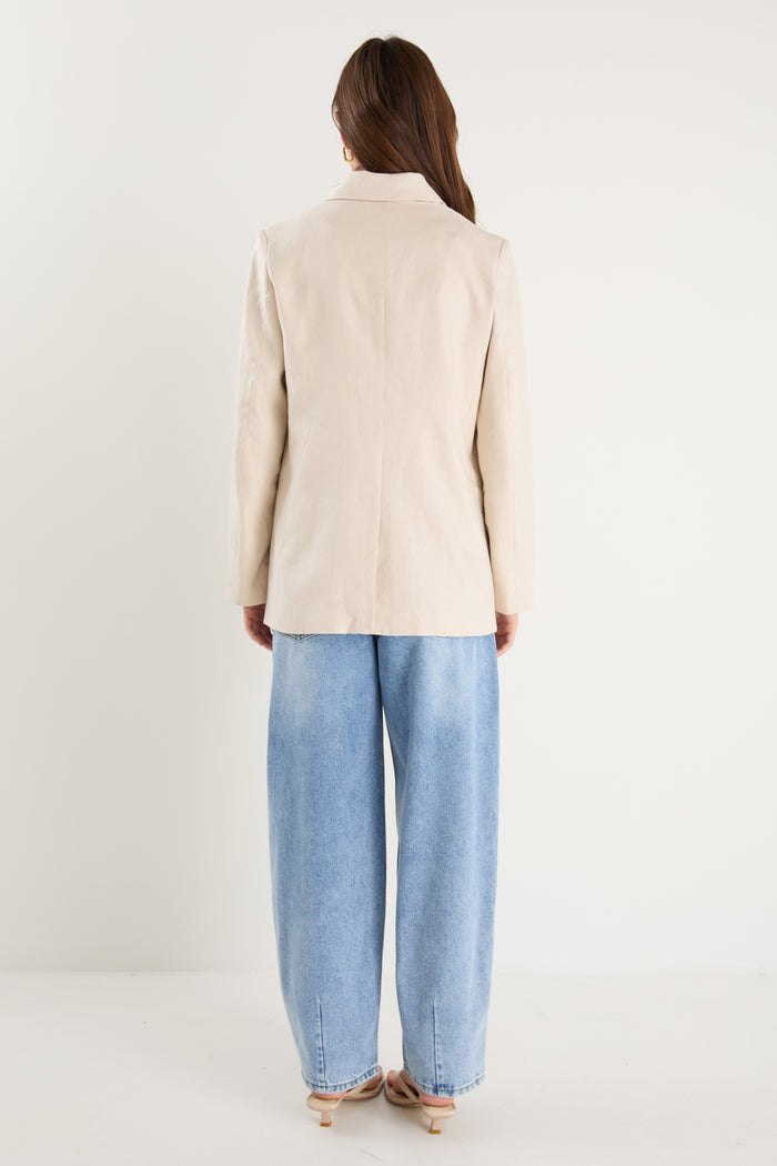 Woman wearing a long-sleeve cream linen blazer with button front and flap pockets, styled with a white top and light blue jeans.
@col_pattern