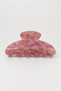 A translucent pink hair claw clip with a marbled pattern, photographed on a seamless light gray background.