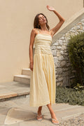 Woman in a yellow dress standing outdoors near a building with stone walls.