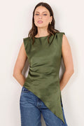 A woman modeling a sleeveless olive green asymmetrical top paired with blue jeans and black sandals, standing against a plain off-white studio background.