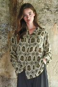 Woman wearing a patterned blouse against a textured stone wall