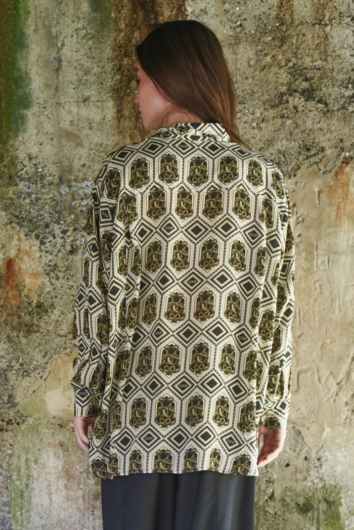 Woman wearing a patterned shirt against a textured wall.