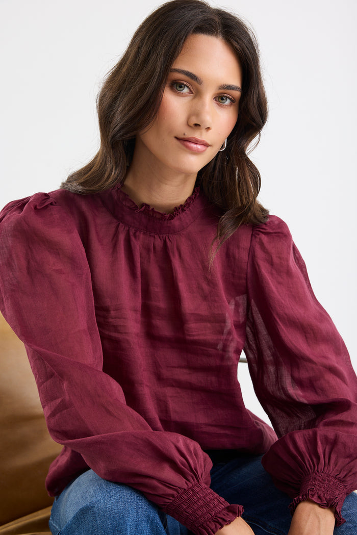 Woman wearing burgundy top on white background.
