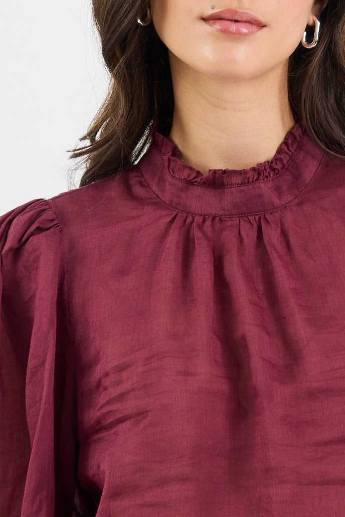 Woman wearing a burgundy blouse with puffed sleeves and blue jeans on a white background