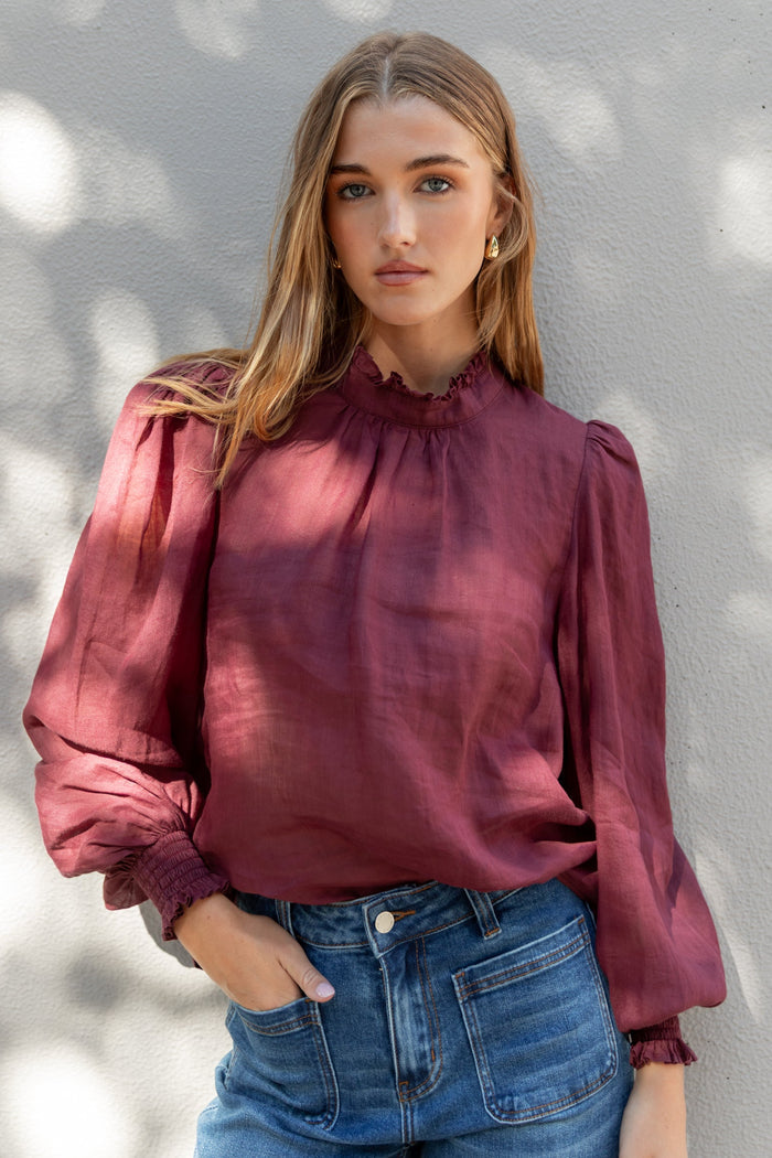 Woman wearing a burgundy blouse and blue jeans against a light background
