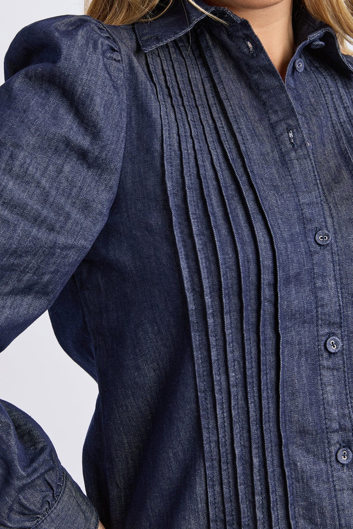 Close-up of a person wearing a dark blue denim shirt with pleated front and puffed sleeves.