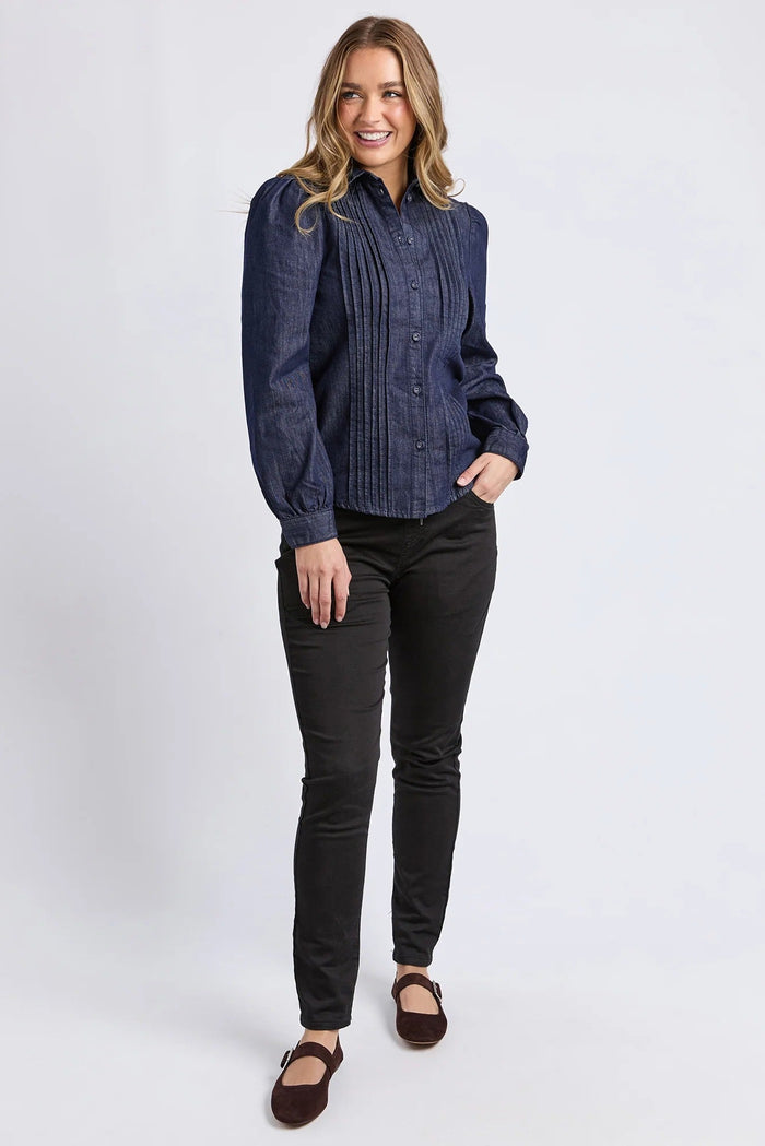 Woman wearing a blue denim shirt and black pants on a white background