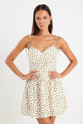 Woman wearing a cream mini dress with khaki polka dots, tiered skirt and tie-up straps, styled with gold jewellery.