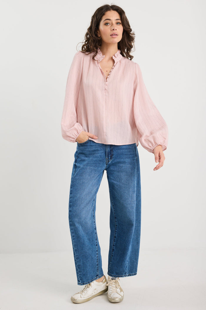 Woman wearing a light pink blouse and blue jeans on a white background