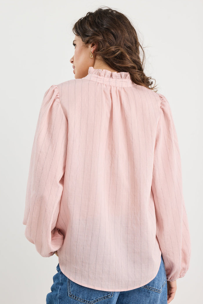 Person wearing a light pink blouse with long sleeves and blue jeans on a white background