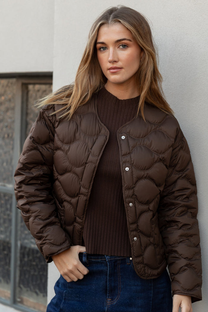 Woman wearing a brown quilted jacket against a light-colored wall.
