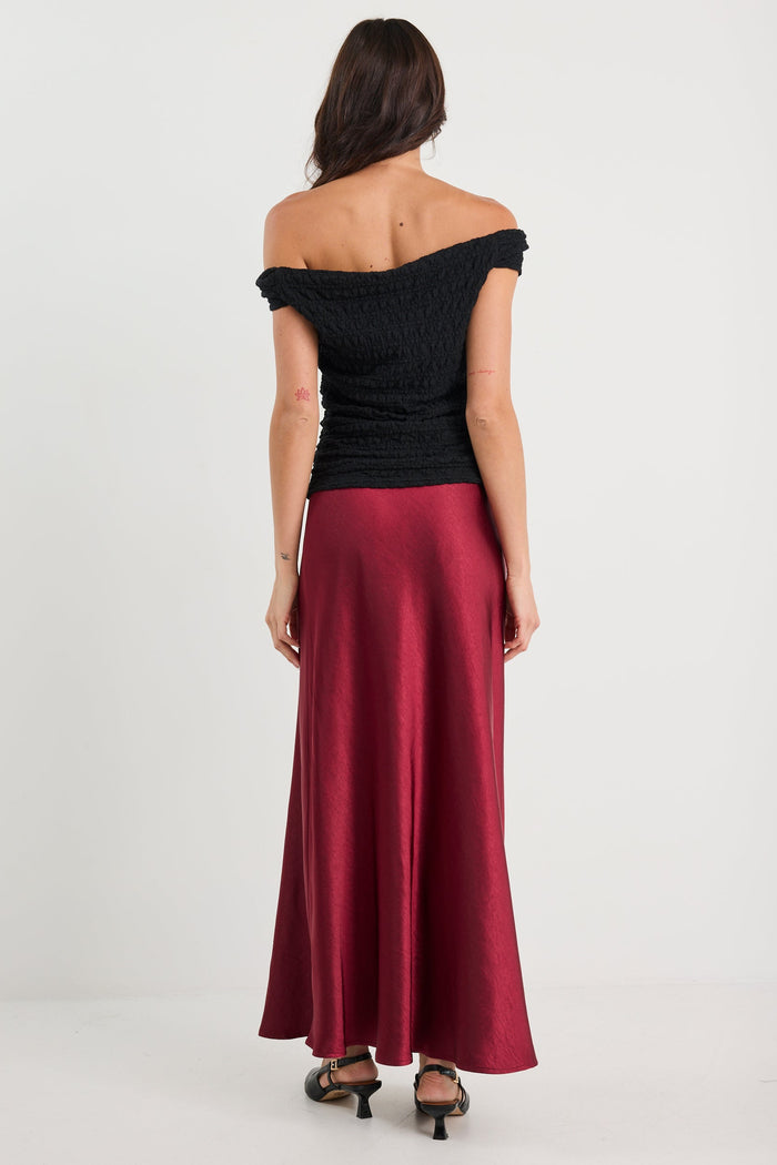 Woman wearing a black off-shoulder top and burgundy skirt on a white background