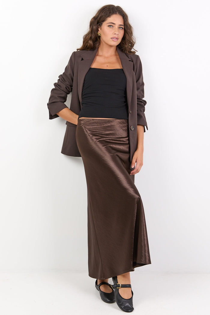 Woman wearing a brown jacket and long skirt on a white background