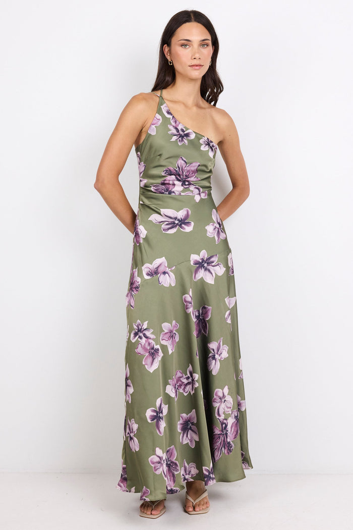 A woman modeling a one-shoulder olive green maxi dress with a purple and white floral print, standing against a plain white studio background.