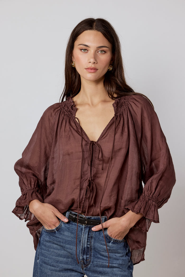Woman wearing a brown blouse and blue jeans against a plain background