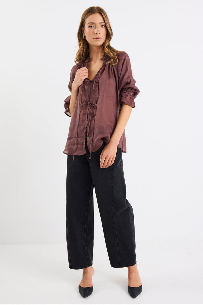 Woman wearing a brown blouse and black pants on a white background