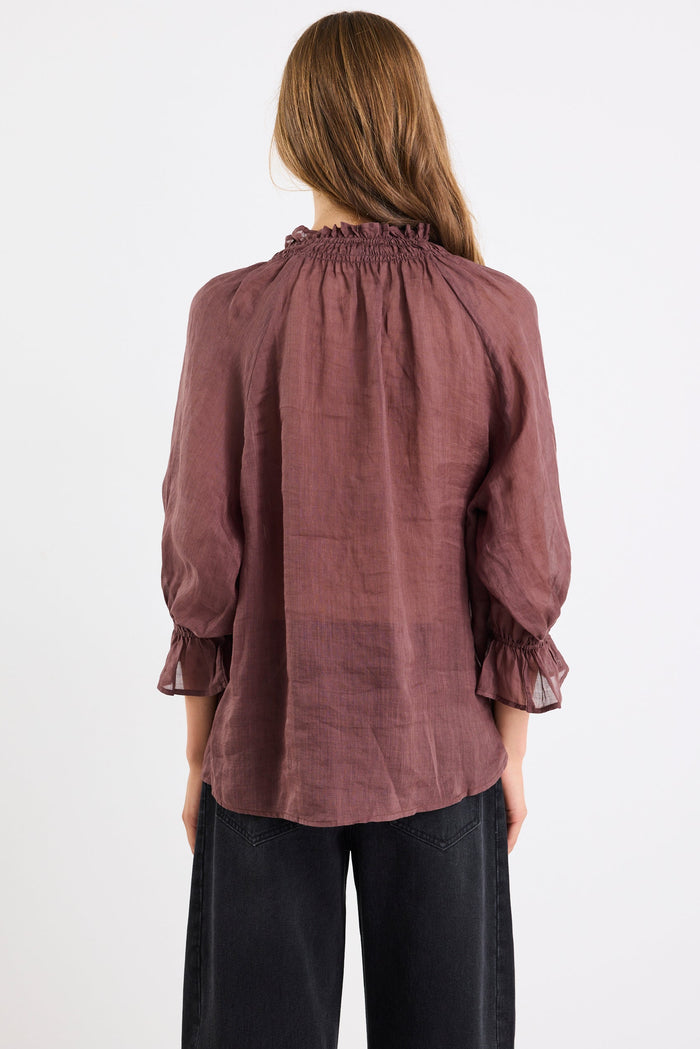 Woman wearing a brown blouse with ruffled sleeves on a white background