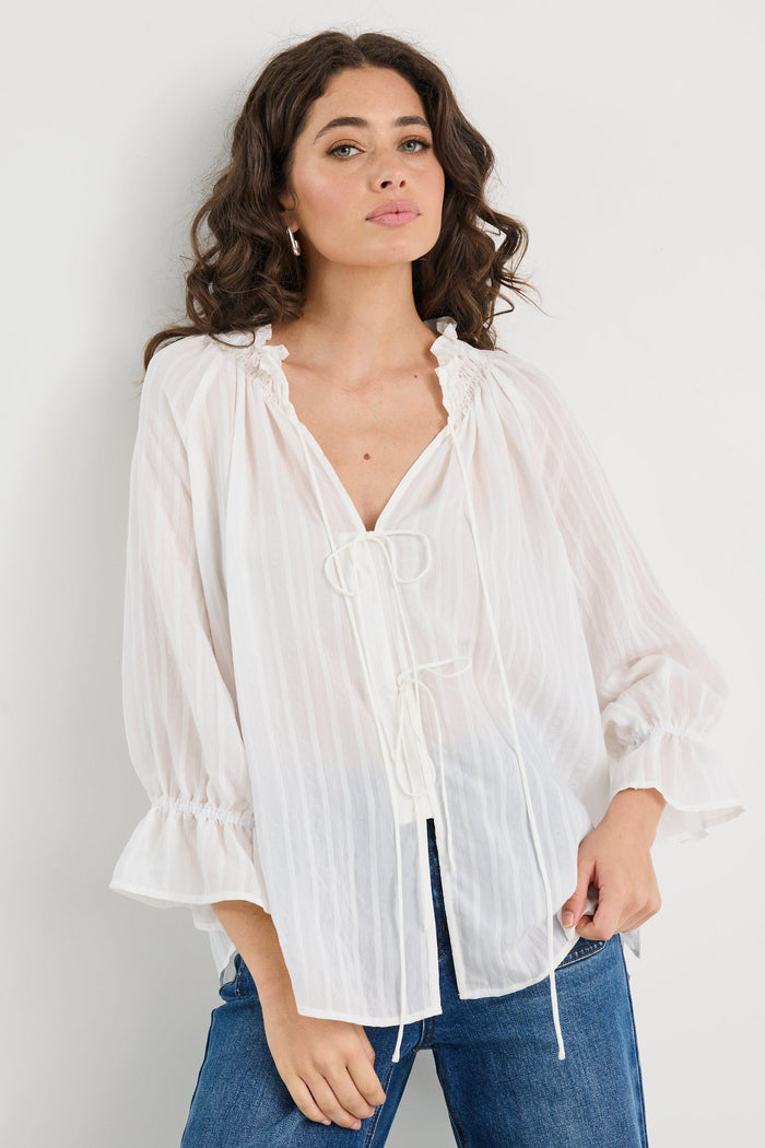 Woman wearing a white blouse and blue jeans against a plain background