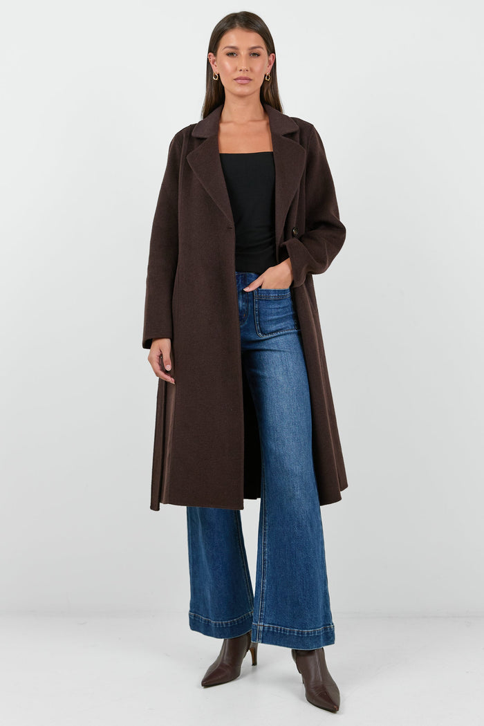 Woman wearing a brown coat, black top, and blue jeans on a white background
