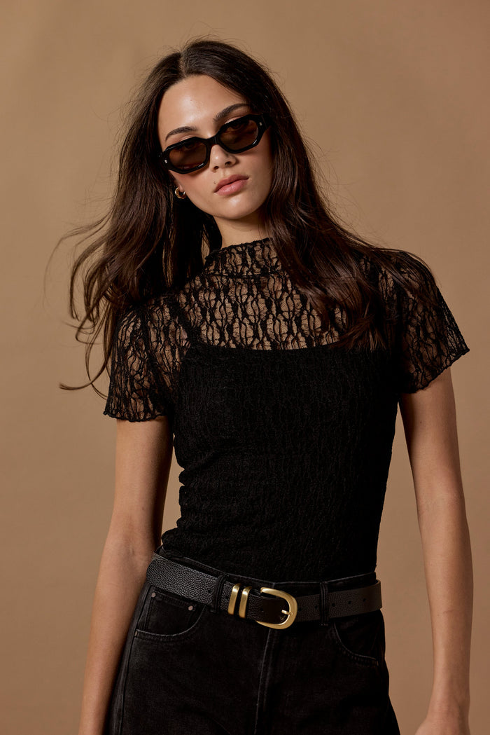 Woman wearing a black lace top and high-waisted black pants against a brown background
