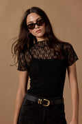Woman wearing a black lace top and high-waisted black pants against a brown background