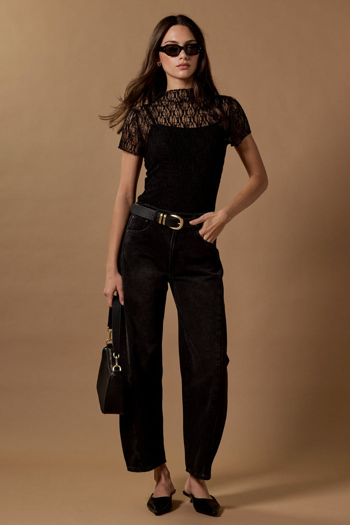 Woman in black outfit with sunglasses and handbag against a brown background