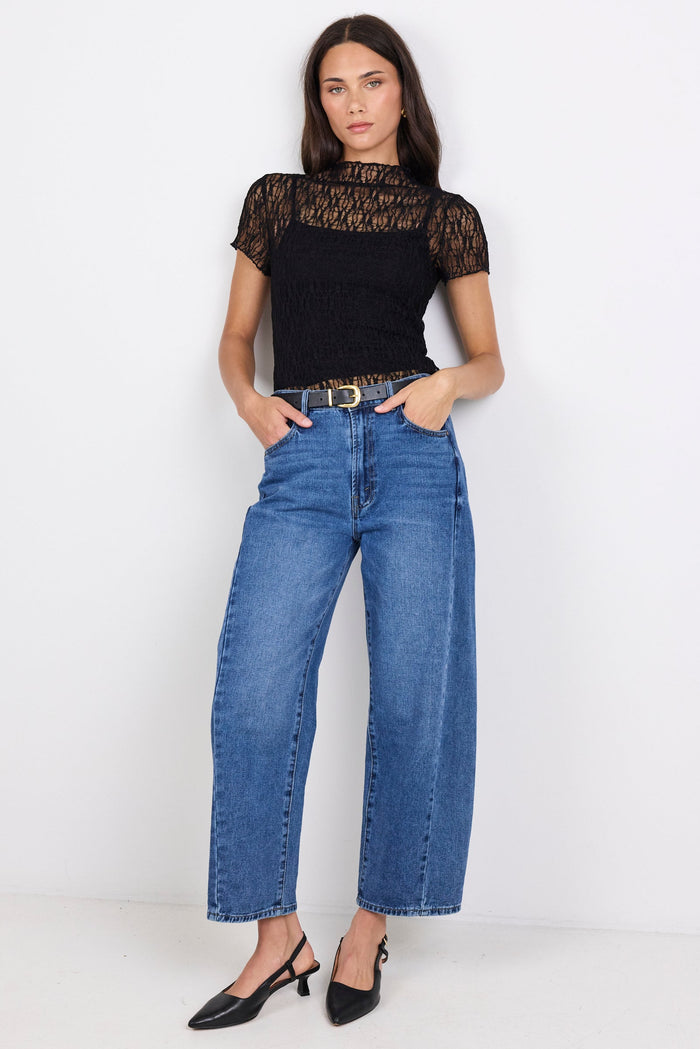 Woman wearing a black lace top and blue jeans on a white background