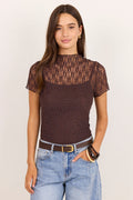 A woman modeling a short-sleeve brown lace and textured knit top with a mock neck, paired with light blue jeans and a brown belt, against a plain off-white background.