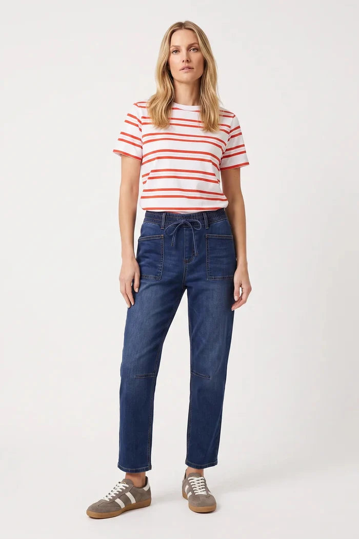 A woman modeling a white short-sleeve t-shirt with thin red horizontal stripes, paired with dark blue high-waisted jeans and brown sneakers, against a plain white studio background.