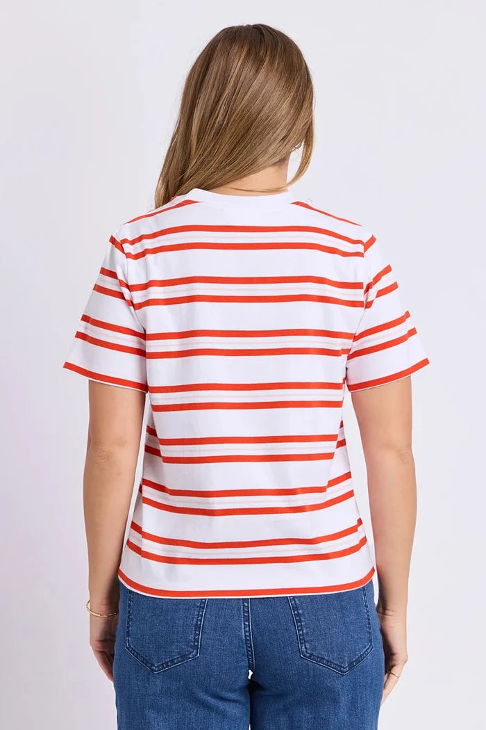 A woman viewed from the back wearing a white short-sleeve T-shirt with thin orange horizontal stripes and blue jeans, against a plain light gray studio background.