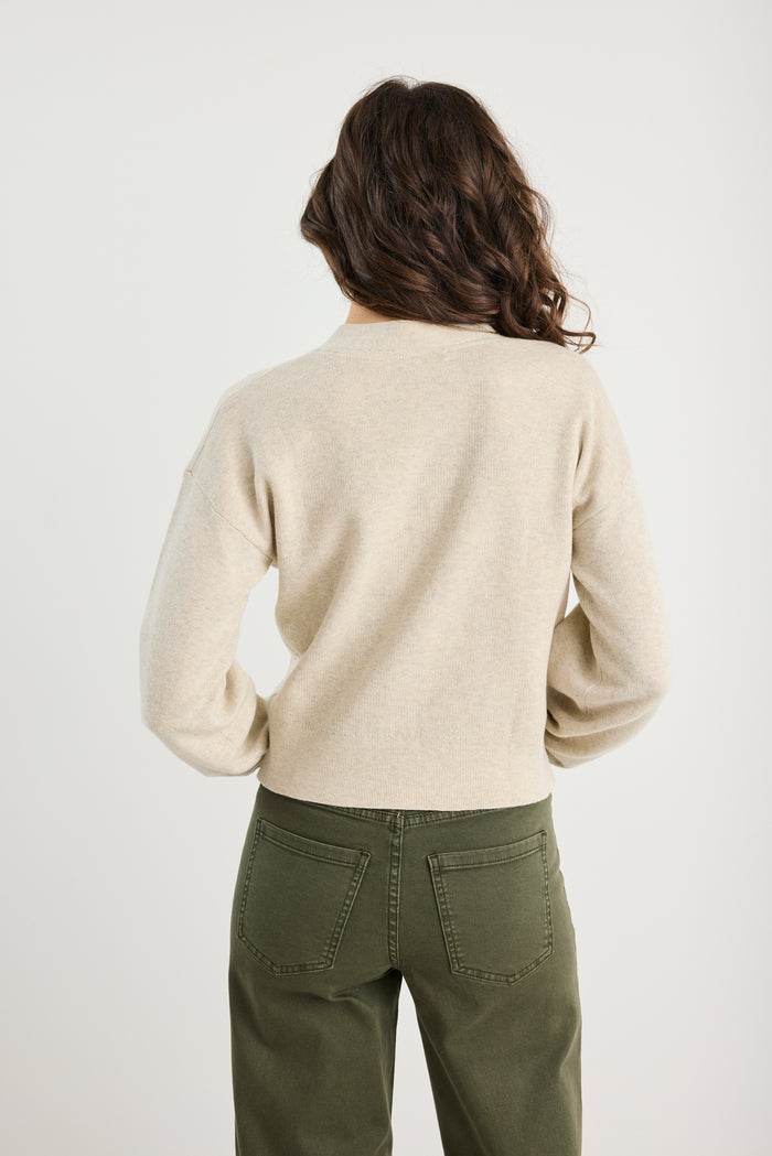 Person wearing a beige sweater and green pants on a white background
@col_pattern