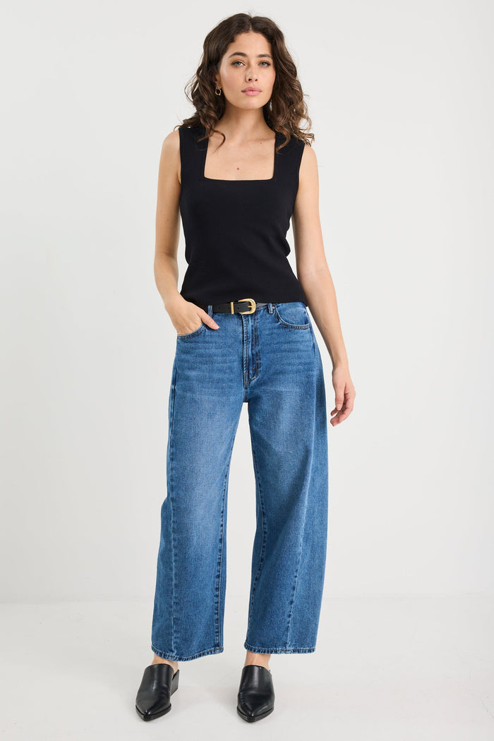Woman wearing a black top and blue jeans on a white background