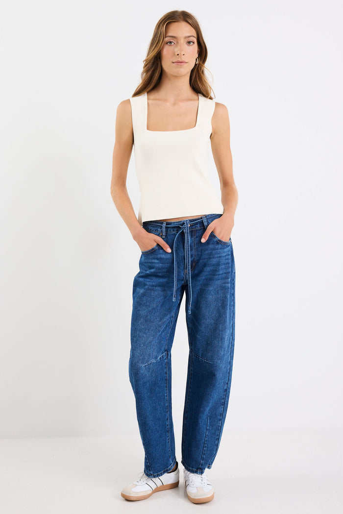 Woman wearing a white tank top and blue jeans on a white background