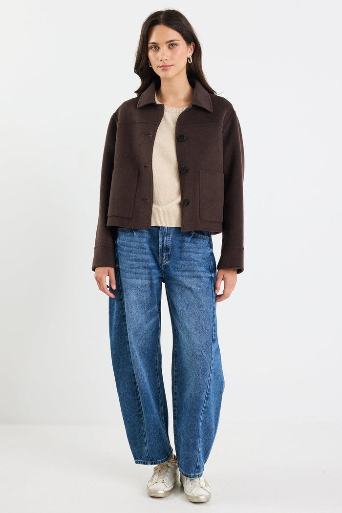 Person wearing a brown jacket, beige top, blue jeans, and white sneakers on a white background