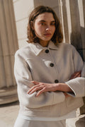 Woman wearing a light-colored coat standing against a neutral background