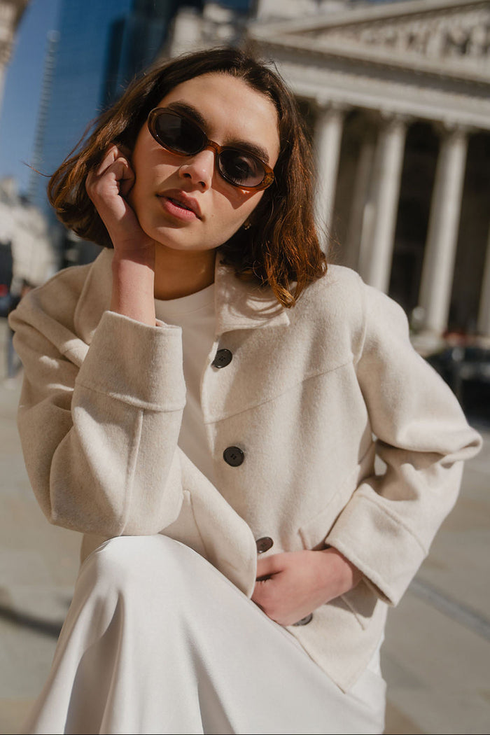 Woman wearing sunglasses and a beige coat in front of a classical building