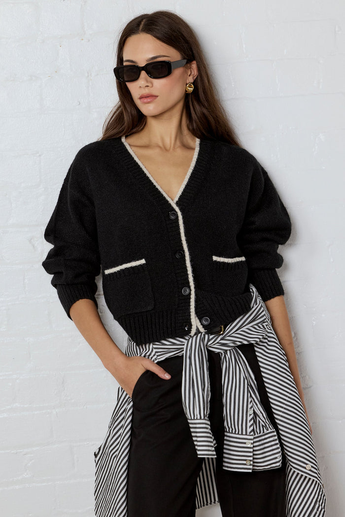 Woman wearing a black cardigan and striped shirt against a white brick wall