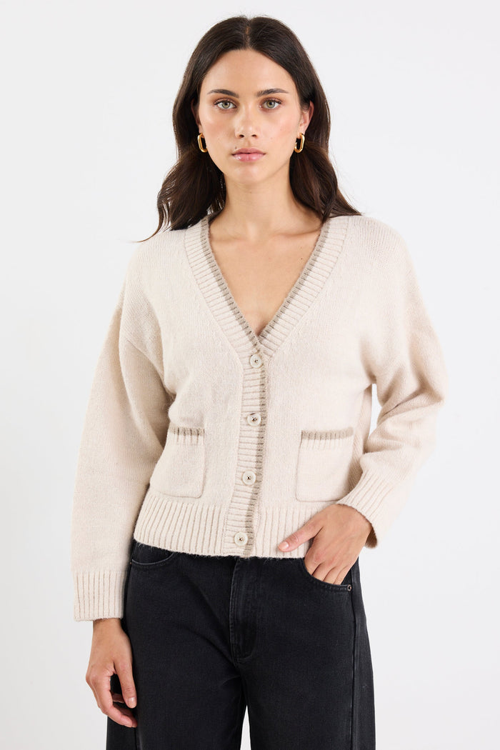 Woman wearing a beige cardigan and black pants on a white background