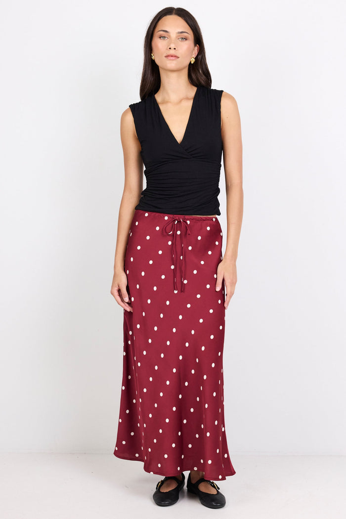 Woman wearing a black sleeveless top and maroon skirt with white polka dots on a white background