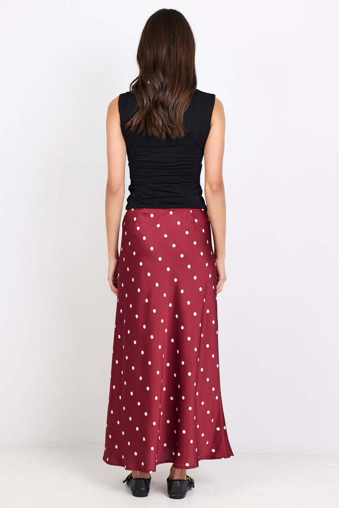 Woman wearing a black sleeveless top and red polka dot skirt on a white background