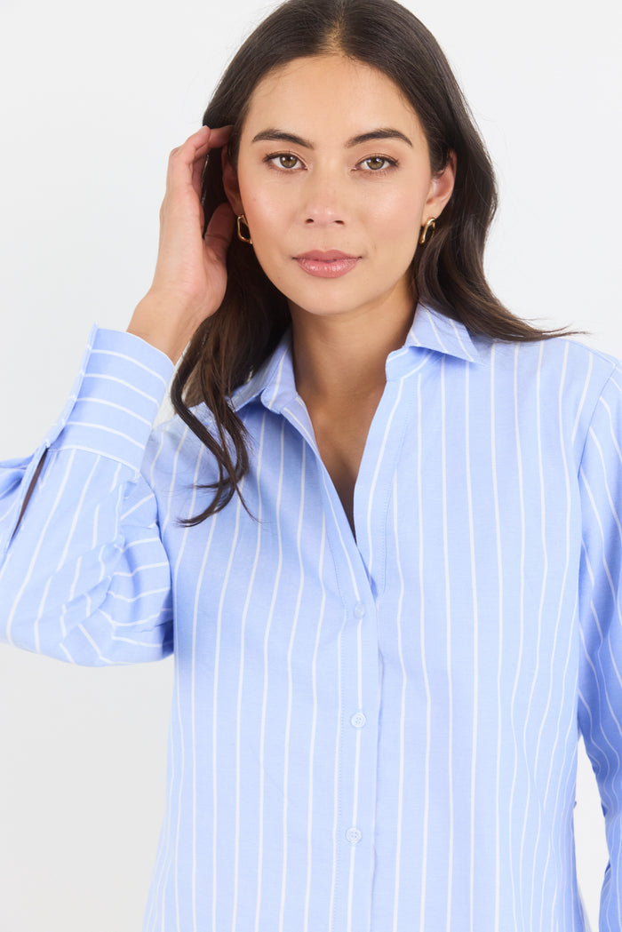 Woman wearing a light blue striped shirt against a plain background